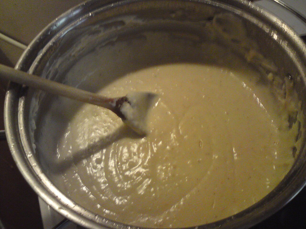 Molho bechamel espesso e liso numa panela de inox, com uma colher de pau mergulhada
