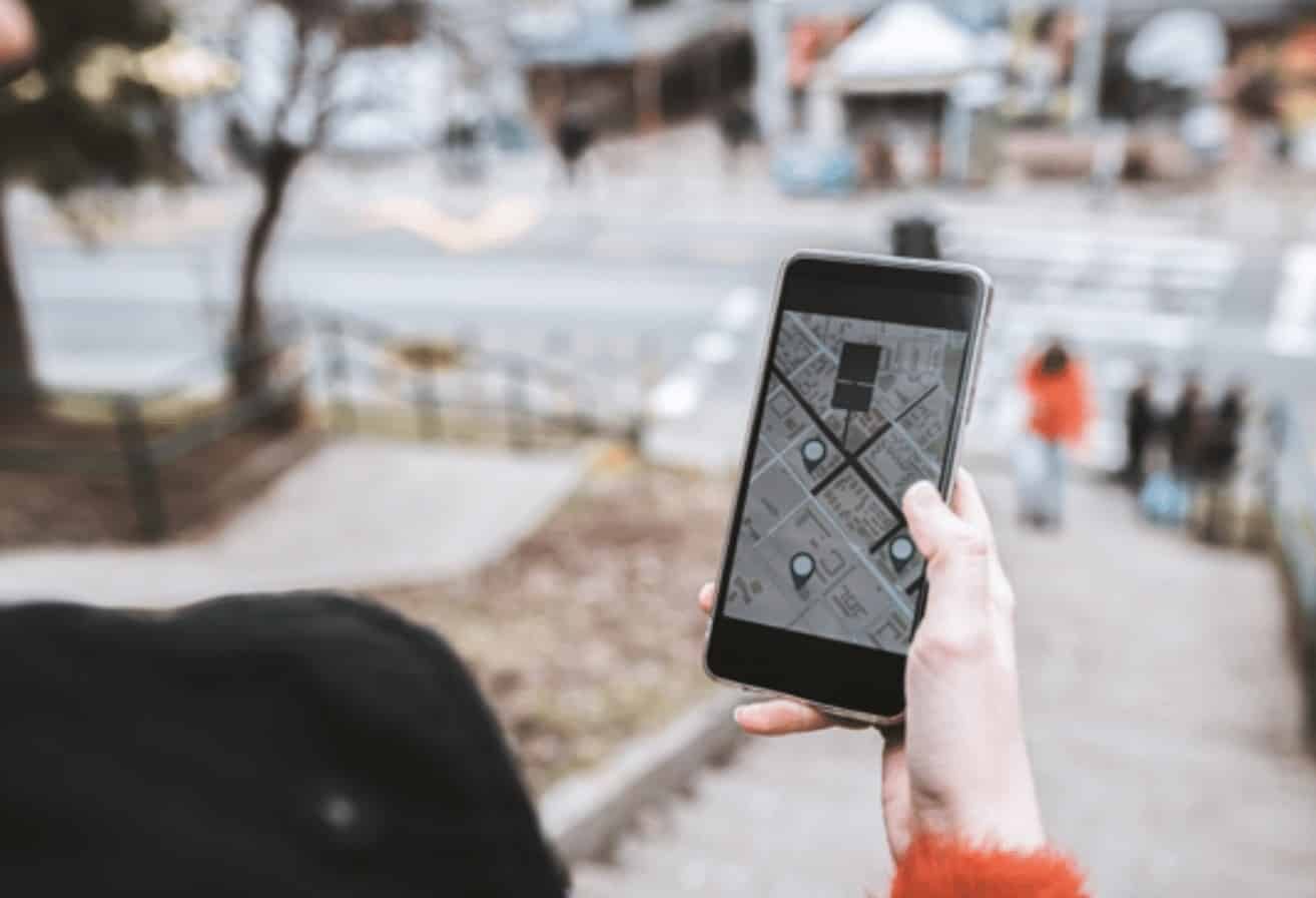Mão segurando celular com aplicativo de mapa aberto numa rua da cidade