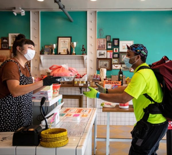 Atendente de máscara entrega pedido a entregador de mochila no balcão de um restaurante
