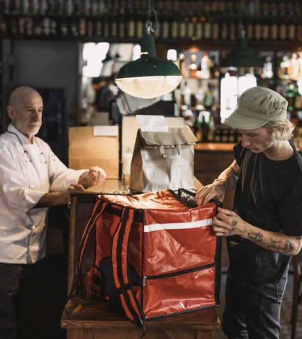 Chef entrega pedido a entregador que guarda a comida numa bolsa térmica vermelha