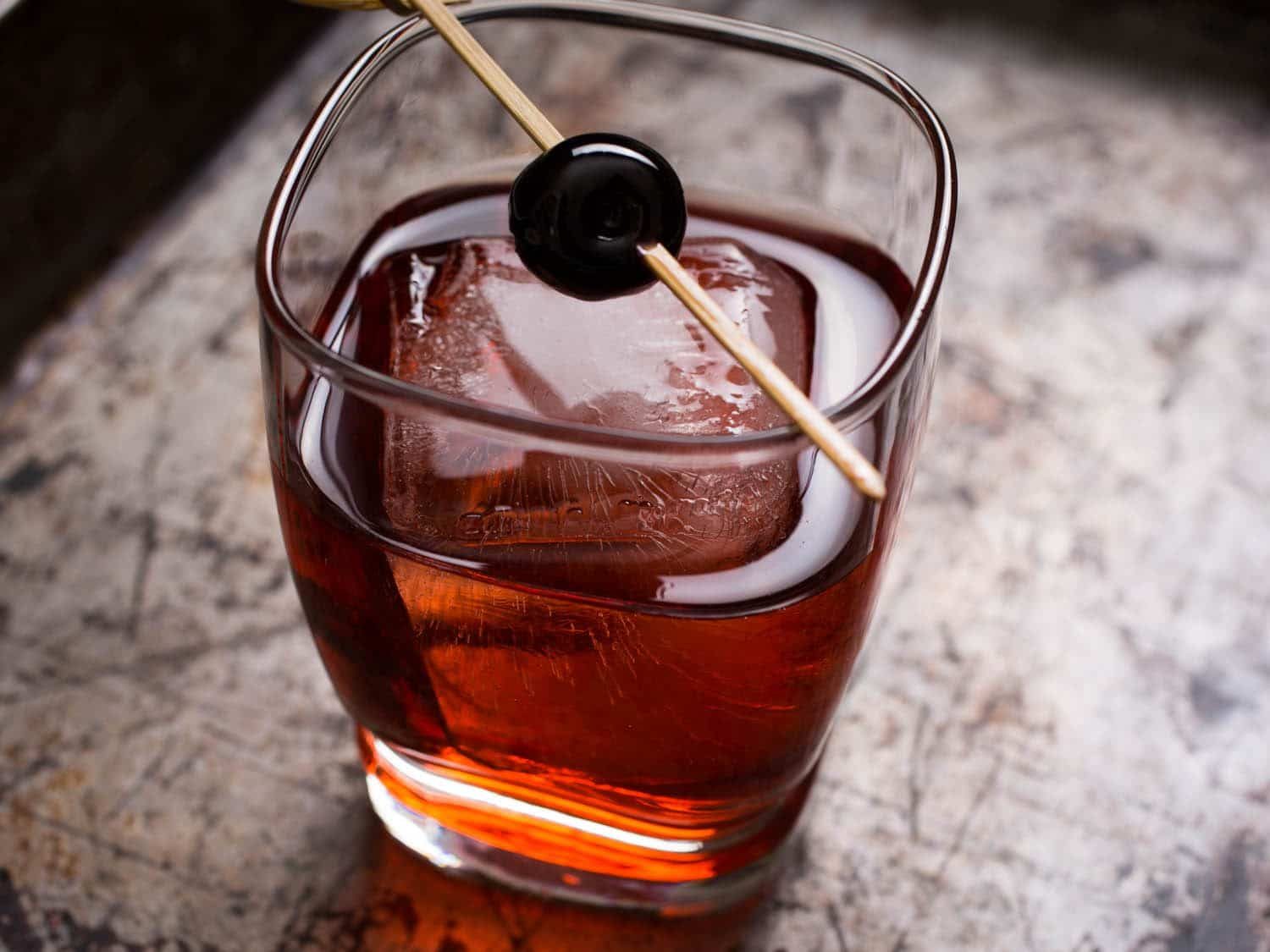 Drink Boulevardier com cubo de gelo e cereja no palito em copo baixo