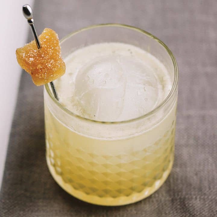 Drink Penicillin com gelo em copo baixo, decorado com gengibre cristalizado no palito
