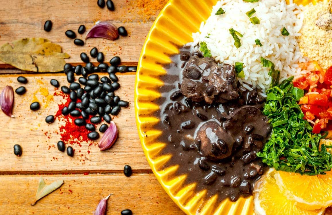 Feijoada servida com arroz, couve refogada, farofa e laranja num prato amarelo