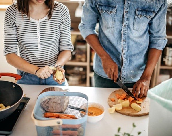 Casal cozinhando em casa, descascando batata e cortando cenoura na tábua
