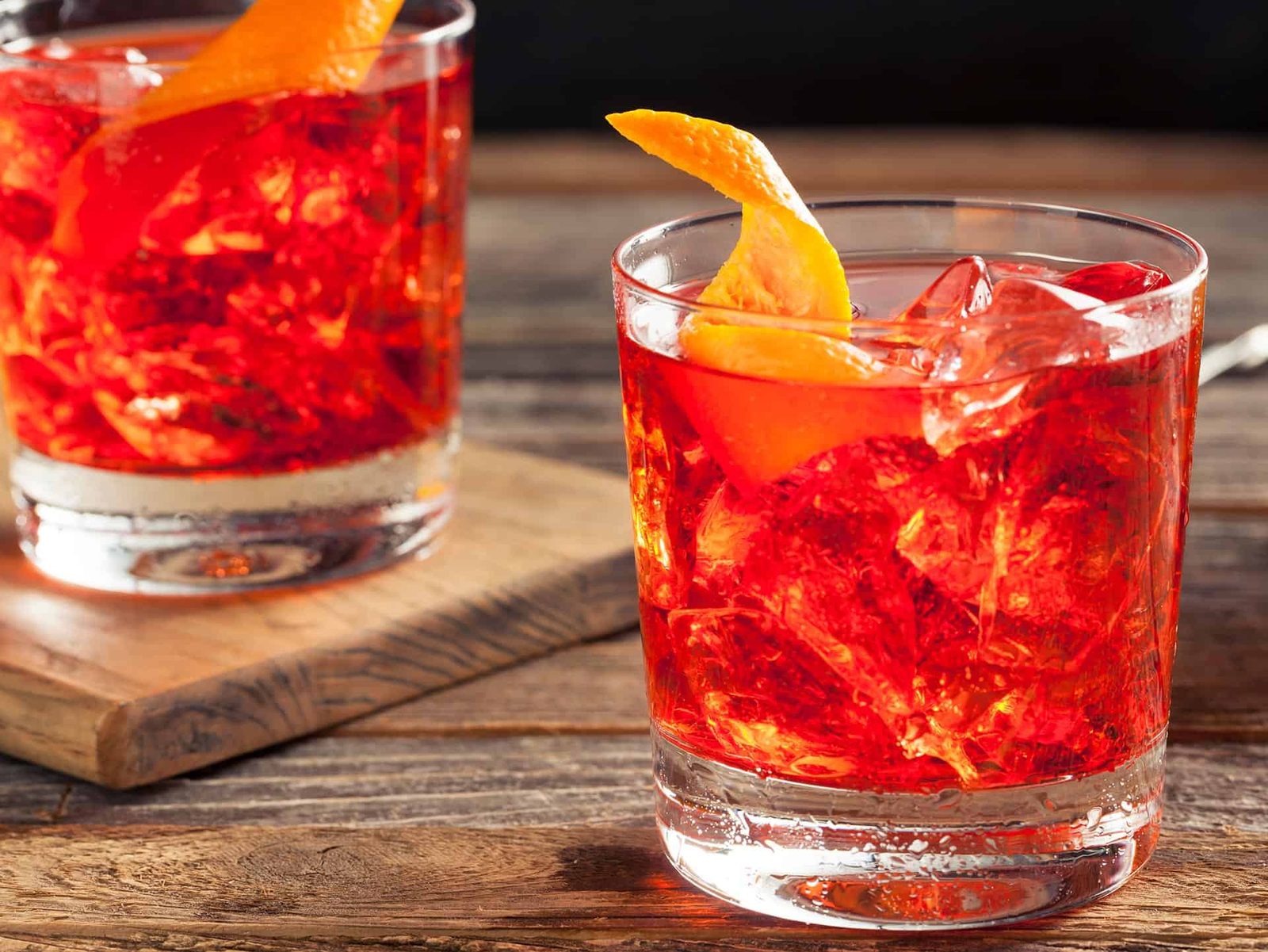 Dois copos de drink Negroni com gelo e casca de laranja sobre mesa de madeira