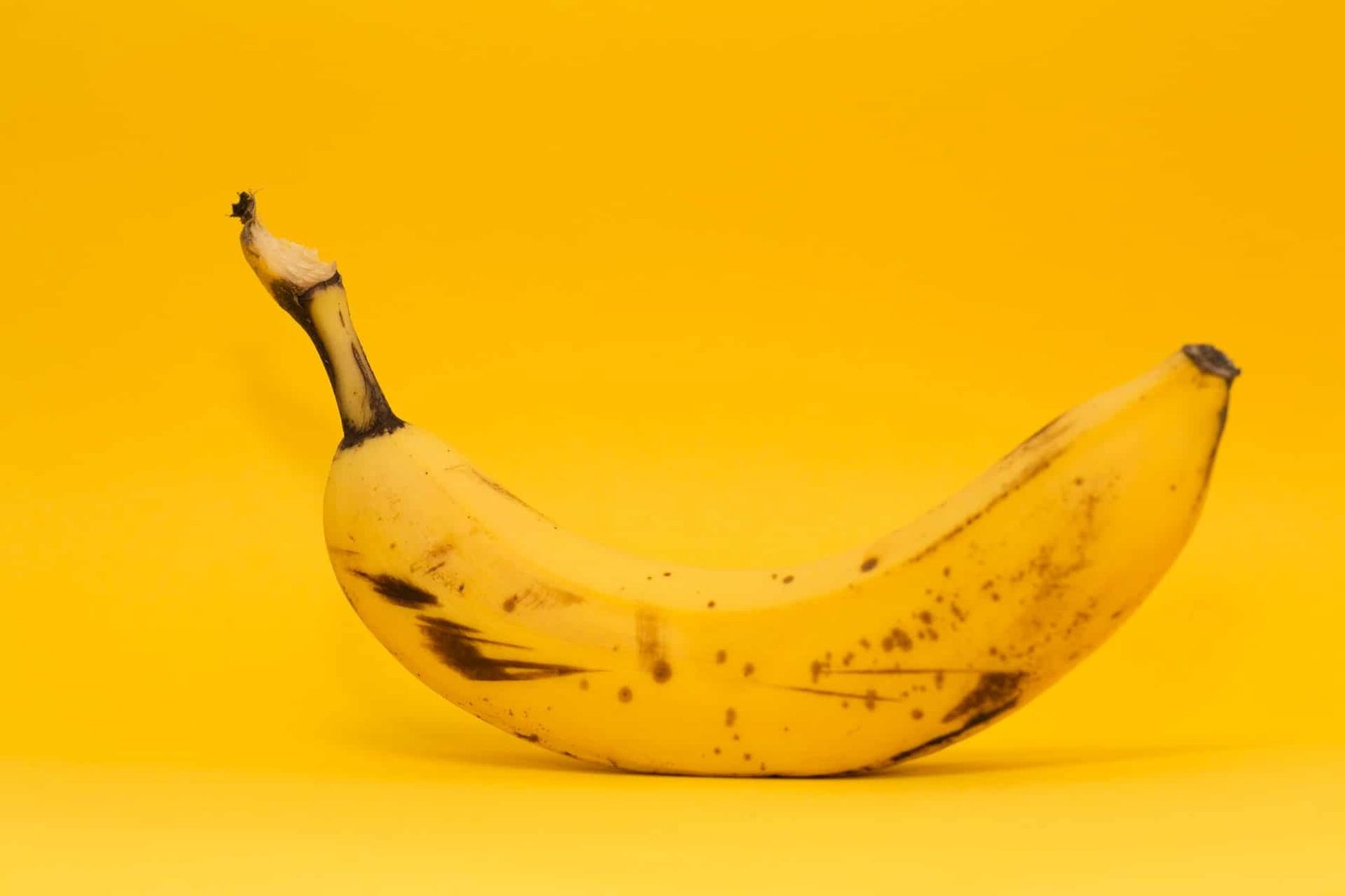 Banana nanica madura com pintas escuras na casca sobre fundo amarelo